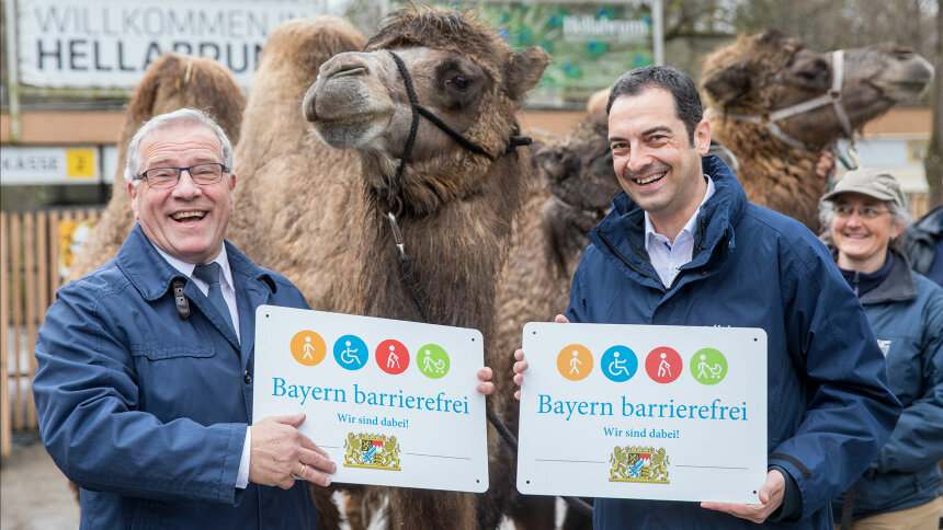 Übergabe des Signets „Bayern barrierefrei“, im Hintergrund zwei Trampeltiere.