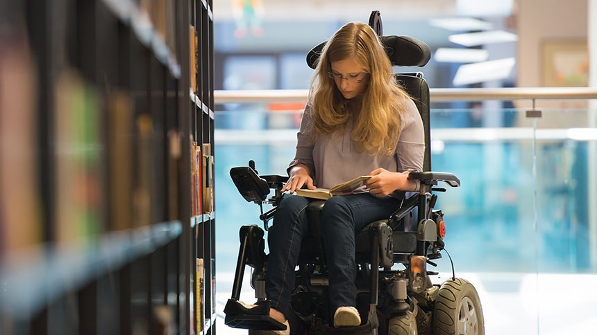 Junge Frau im Elektro-Rollstuhl in einer Bibliothek.