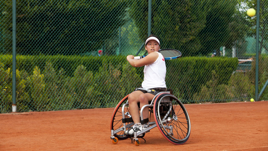 Junge Frau im Sportrollstuhl beim Tennisspielen.