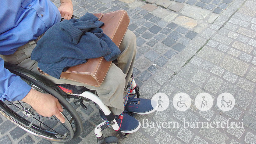 Mann im Rollstuhl auf Gehweg mit unterschiedlicher Pflasterung.