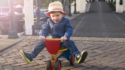 Kleines Kind mit Hut auf Dreirad.