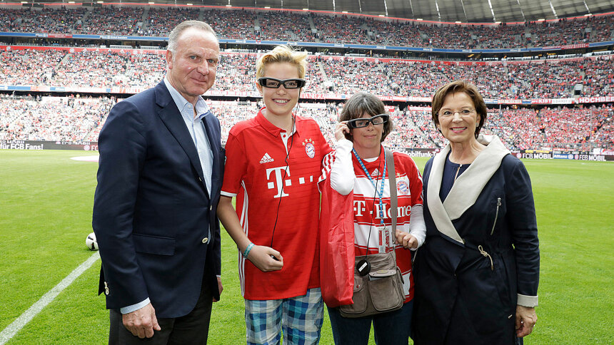 Gruppenfoto: zwei hörbehinderte Fans in der Allianz Arena mit Emilia Müller und Karl-Heinz Rummenigge.