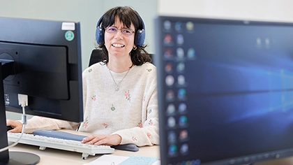 Maria Hütter-Songailo sitzt mit Kopfhörern an ihrem PC-Arbeitsplatz.