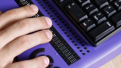 Nahaufnahme: Eine Hand liegt auf einer Braille-Zeile.  
