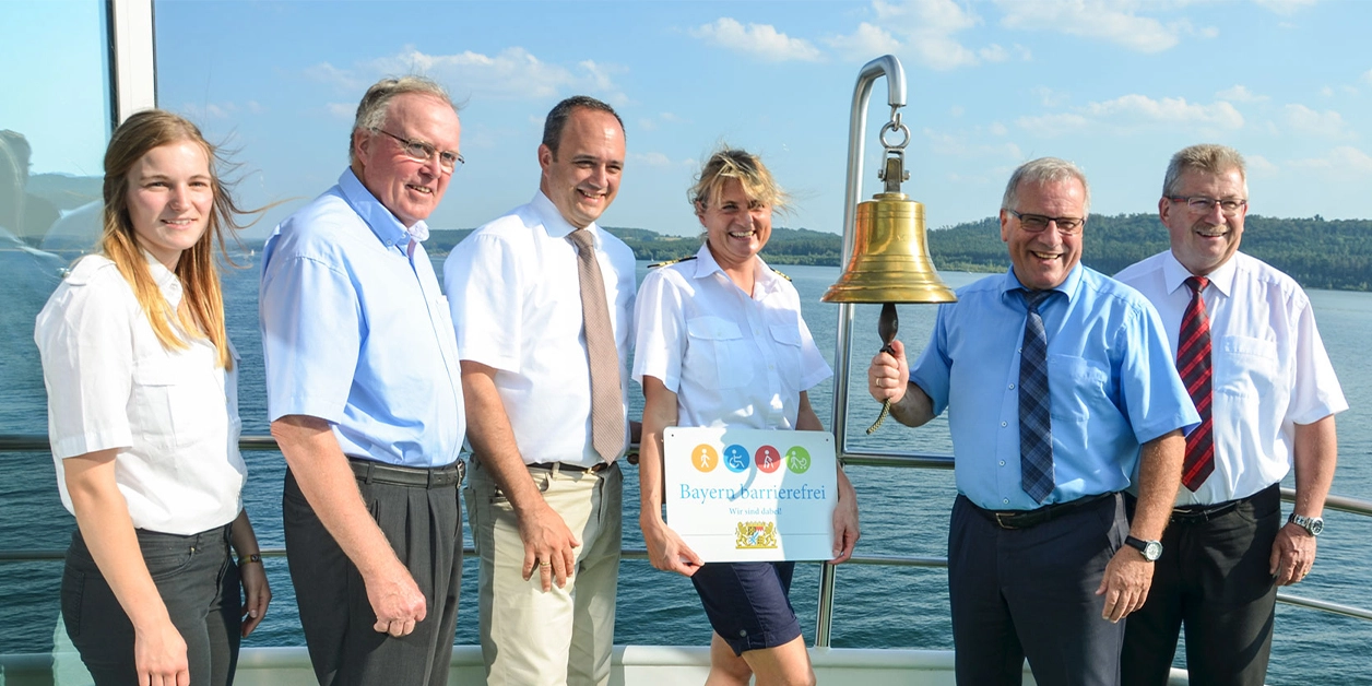 Gruppenbild: Übergabe des Signets „Bayern barrierefrei“ auf einem Ausflugsschiff.