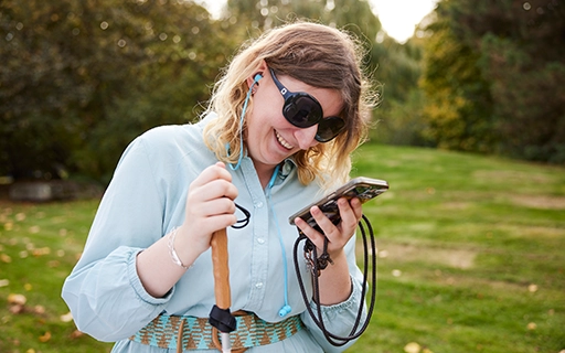 Eine Frau mit Sonnenbrille schaut lächelnd auf ihr Smartphone. 