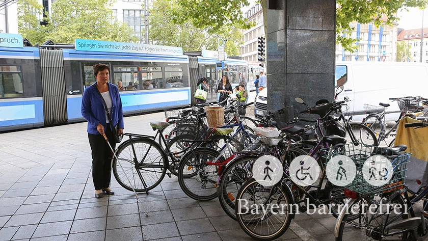 Frau mit Langstock stößt an Fahrrad.