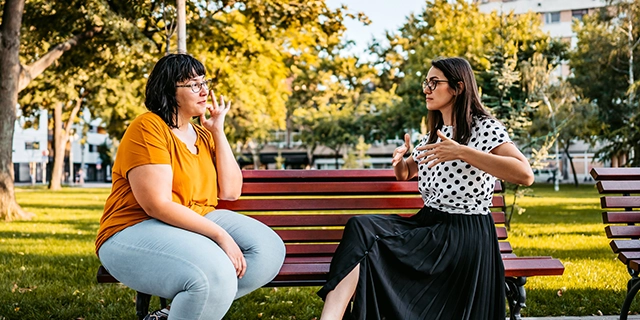 Zwei Frauen sitzen auf einer Bank. Sie unterhalten sich.