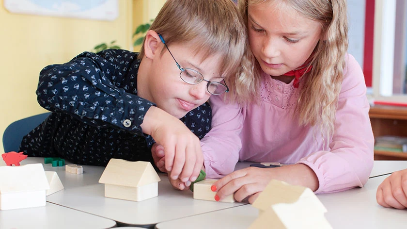 Zwei Kinder, eines mit Down-Syndrom, spielen mit Bauklötzen.