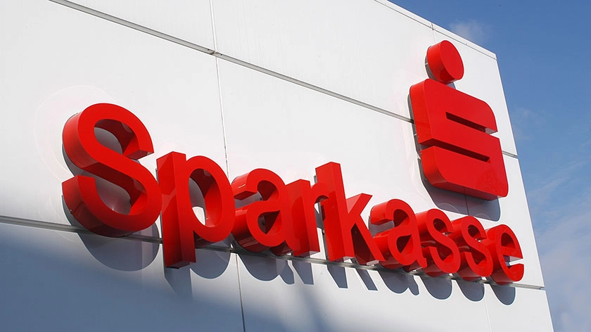 Nahaufnahme: Schriftzug „Sparkasse“ mit Logo an Gebäudefassade.