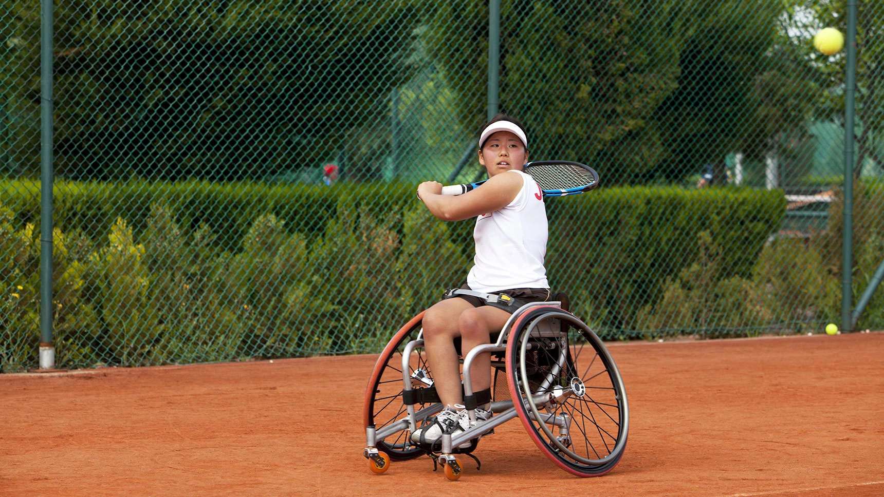 Junge Frau im Sportrollstuhl beim Tennisspielen.