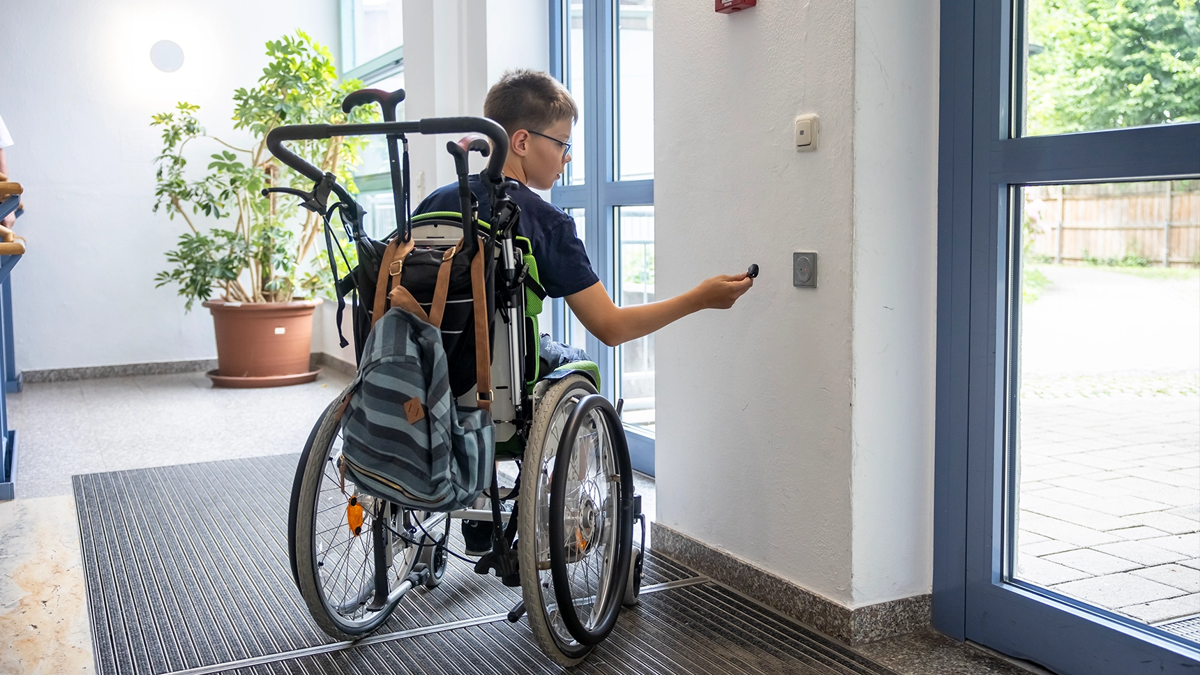 Ein Schüler im Rollstuhl öffnet eine automatische Tür am Ausgang der Schule.