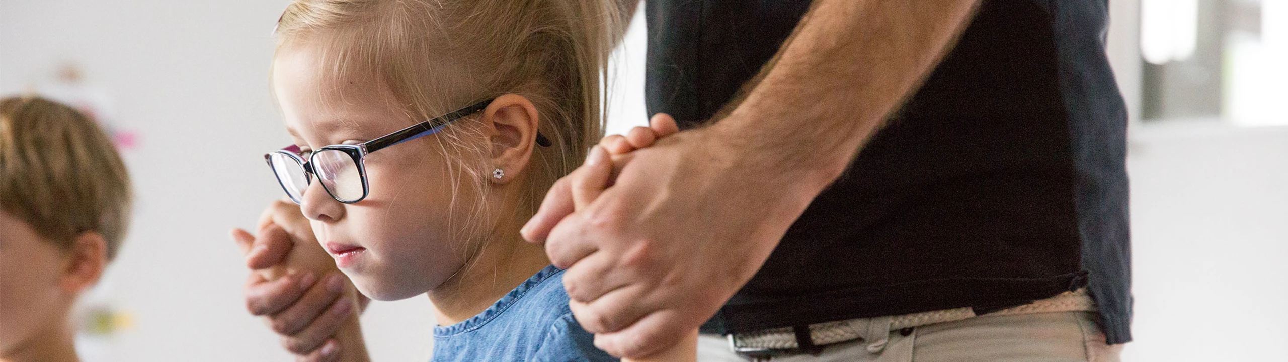 Nahaufnahme: Ein kleines Mädchen steht im Raum; ein junger Mann hält es an beiden Händen.