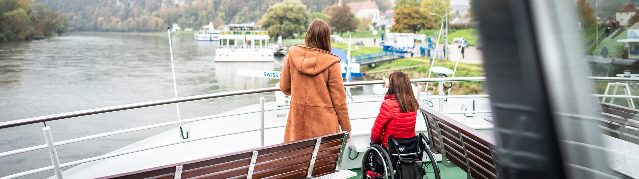 Eine Mutter steht mit ihrer Tochter im Rollstuhl auf einer Fähre.