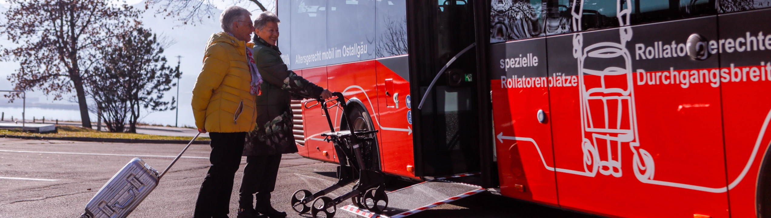 Einer Frau mit Rollator und einem Mann mit Koffer wird der Einstieg in den Bus mithilfe einer Rampe erleichtert. 