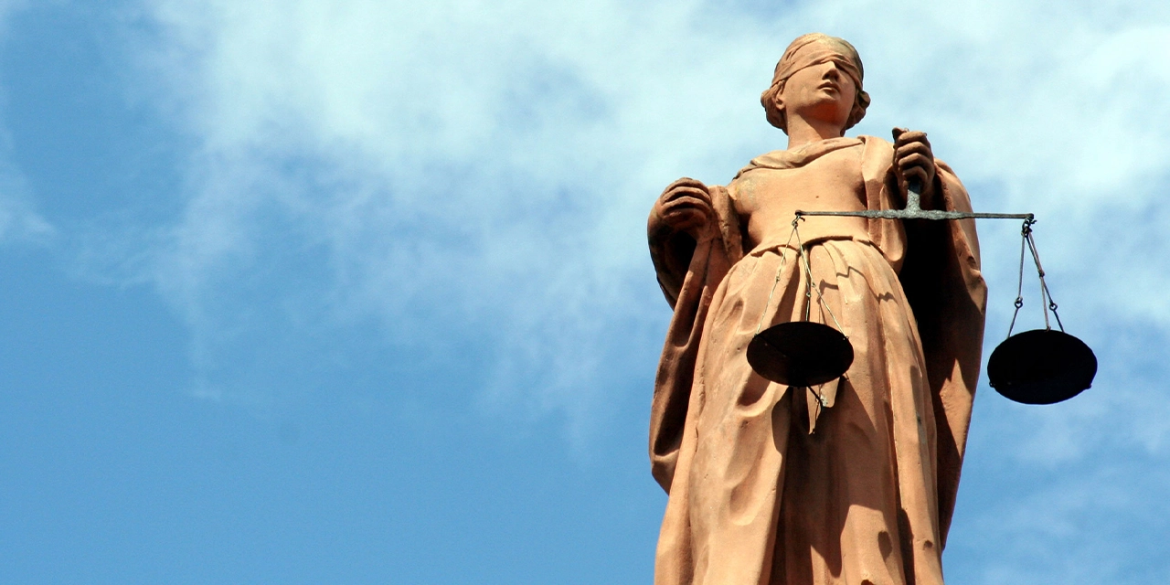 Statue der Justitia, dem antiken Symbol der Gerechtigkeit: eine Frauenfigur mit verbundenen Augen und einer Waage in der linken Hand.